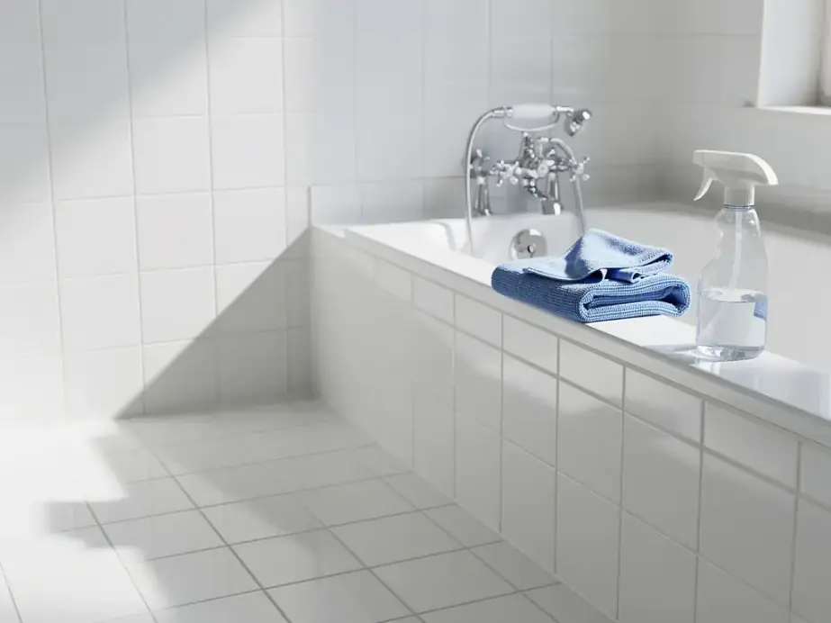 Deep-cleaned bathroom with bright grout, a chrome tap and a microfiber cloth on the tub edge