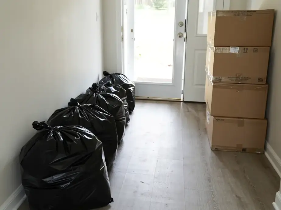 Hallway mid clean-out with tied contractor bags and sealed boxes by the open front door