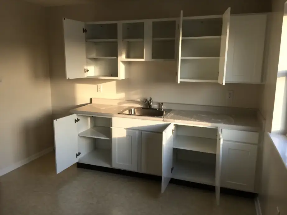 Empty apartment kitchen with open, emptied cabinets and bare counters after a move-out clean
